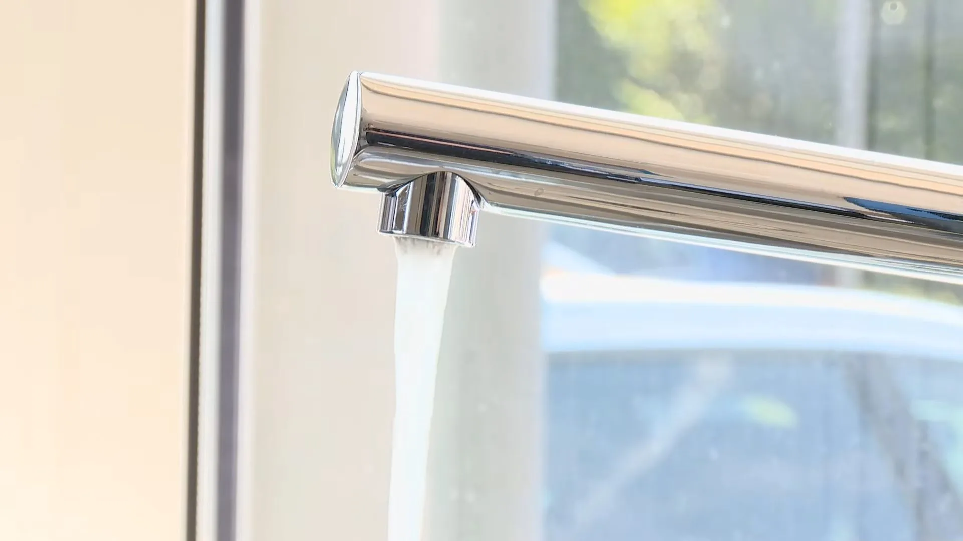 A chrome kitchen faucet running a steady stream of water beside a window