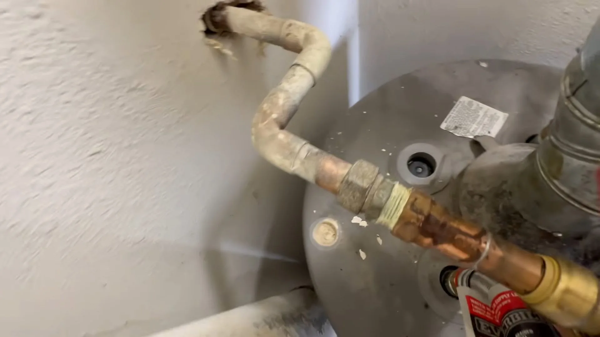 A copper and brass fitting joining a water line to the side of a gray water heater tank