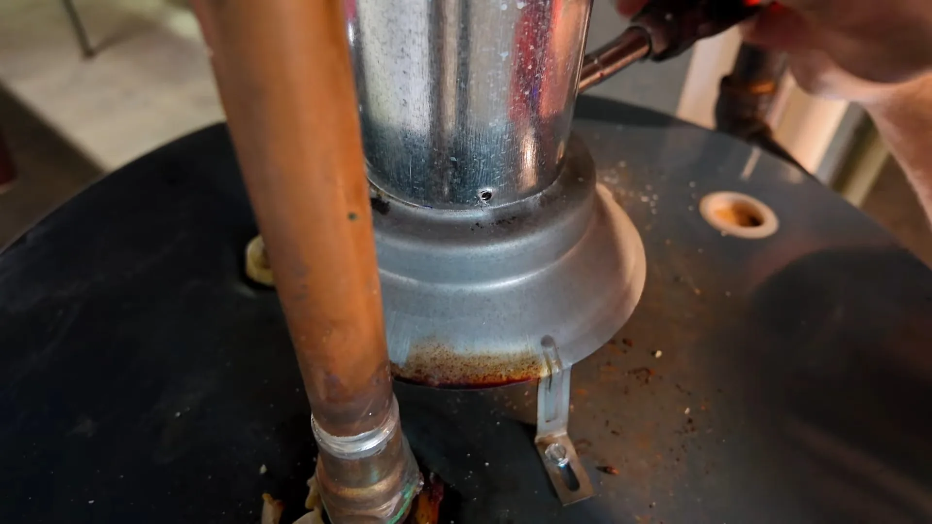 A copper pipe and a metal vent flue rising from the top of a black water heater tank