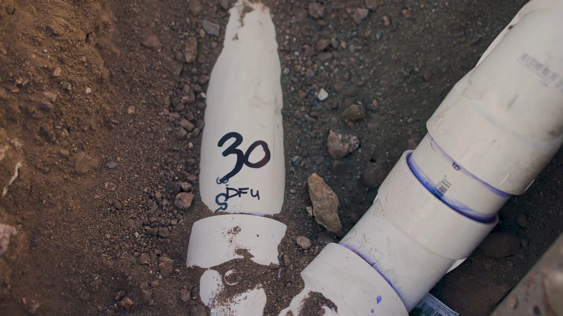 White PVC drain pipes cut into soil with a handwritten number marked on one of them