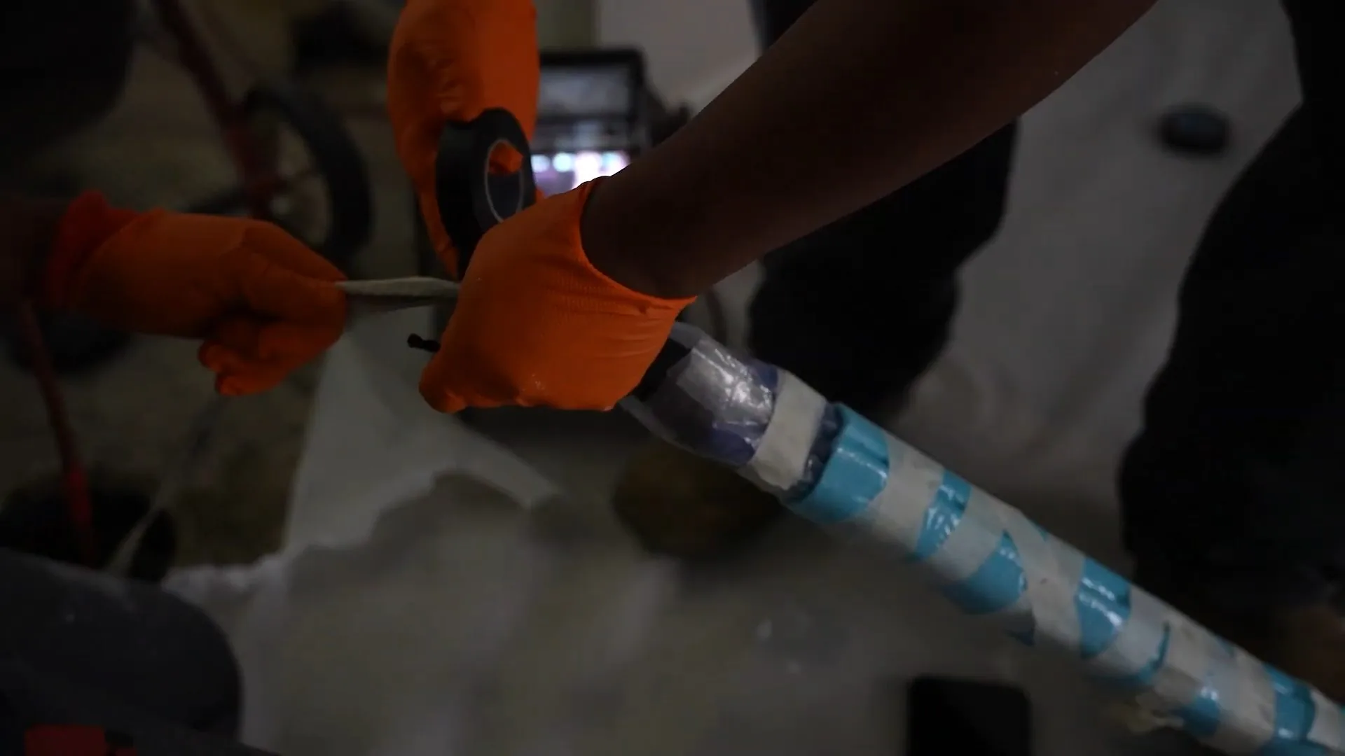 Hands in orange gloves handling a long liner tube wrapped with blue tape