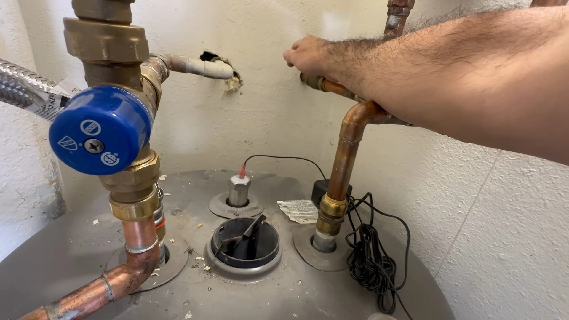 An arm adjusting a copper pipe on top of a water heater beside a blue-handled valve