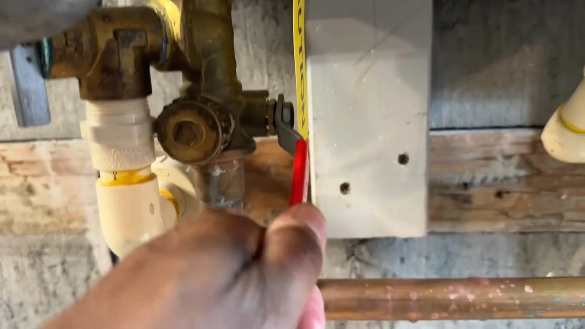 A hand holding a tape measure against brass valves and white pipes on a wall