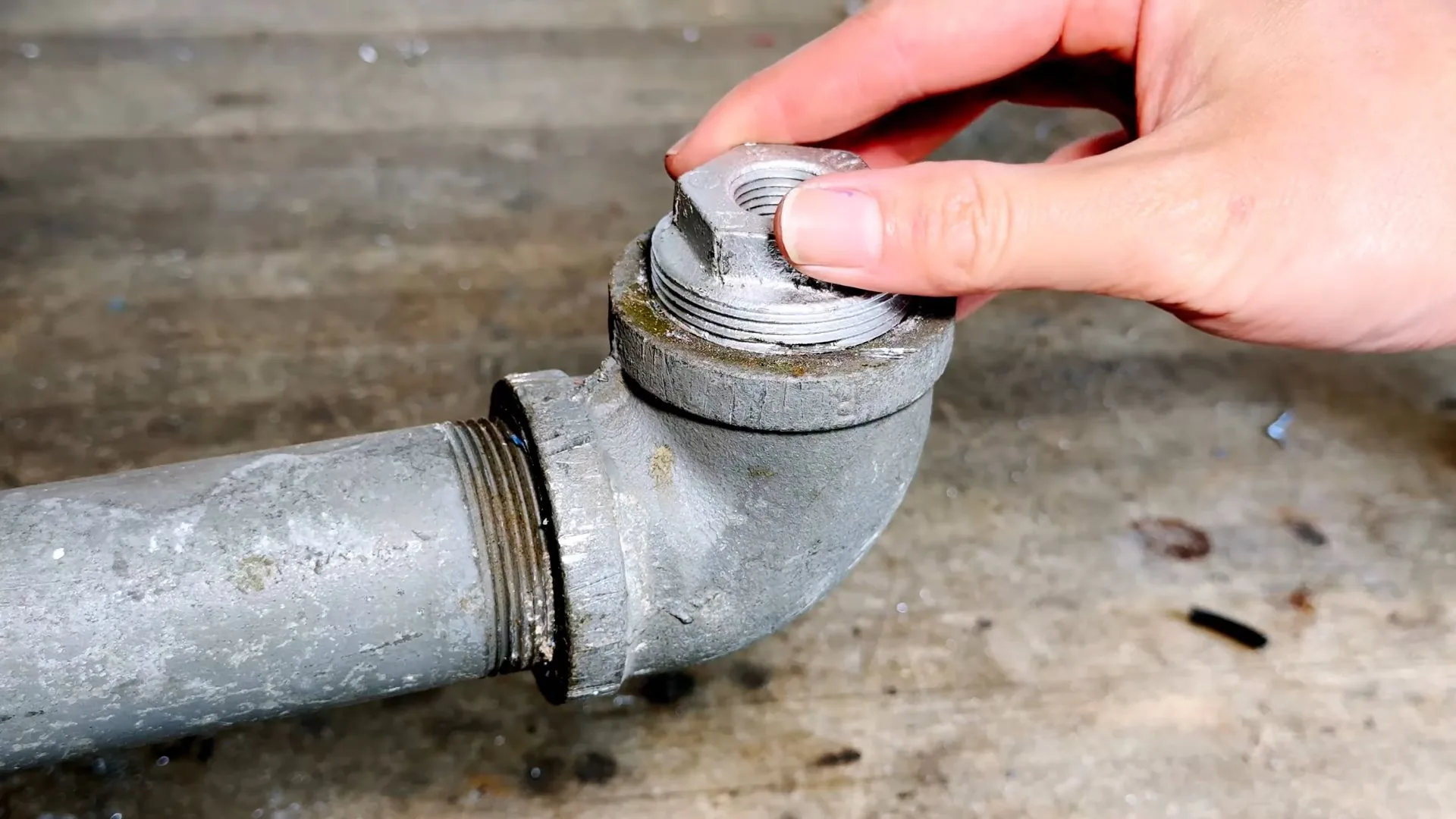 A hand unscrewing a threaded cap from a gray cast iron cleanout elbow