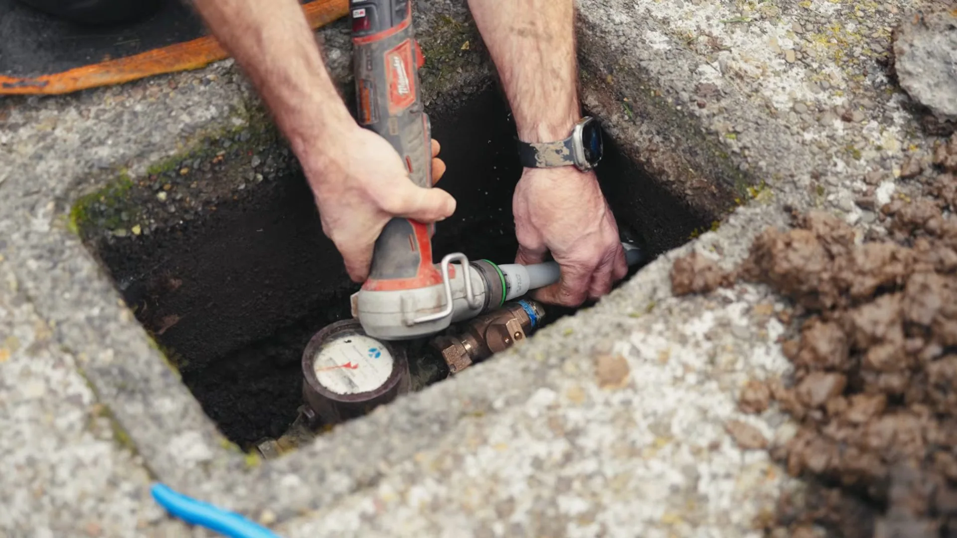 Hands working beside a water meter and a brass valve inside an open in-ground box