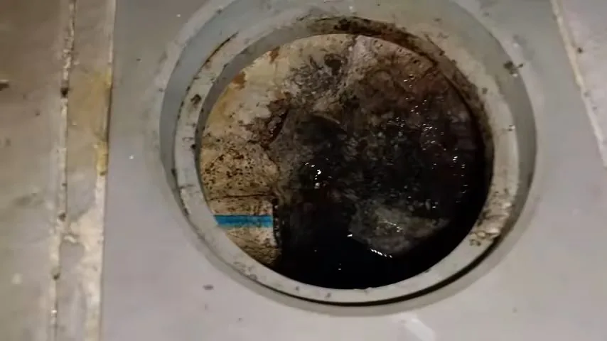 A round opening in a gray floor with dark residue on the wall and standing water inside
