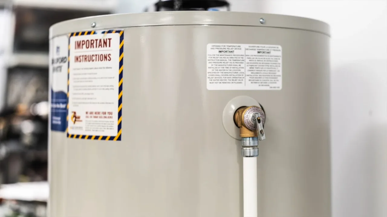A tank water heater showing an instructions label and a brass relief valve with a white discharge line