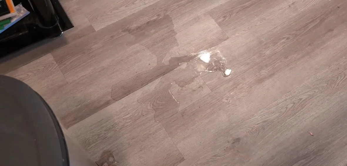 A small puddle of water on a gray wood-look floor