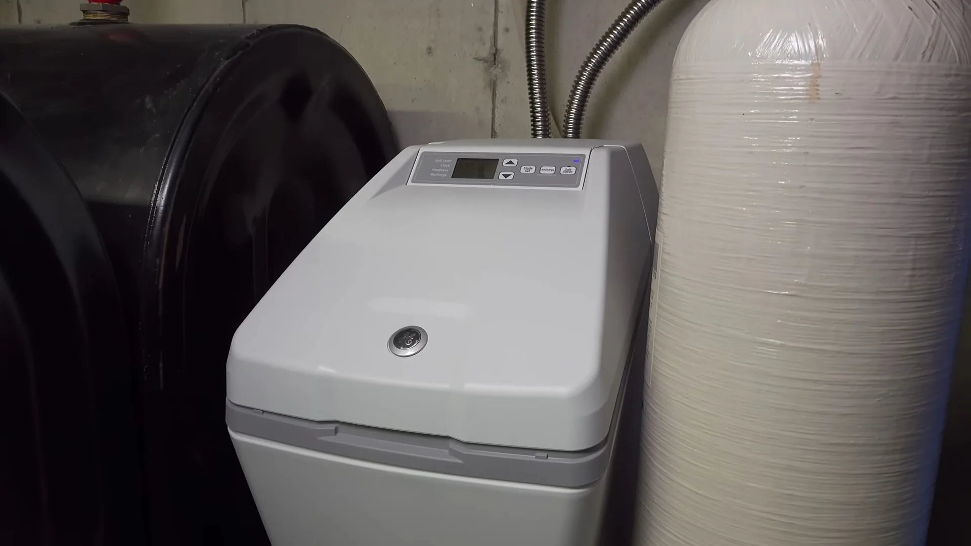 A gray water softener beside a black brine tank and a white resin tank in a utility area